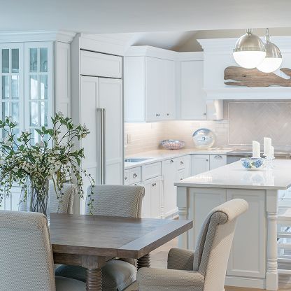 Bright white kitchen and dining nook with gray chairs, wood table, and island under pendant lights