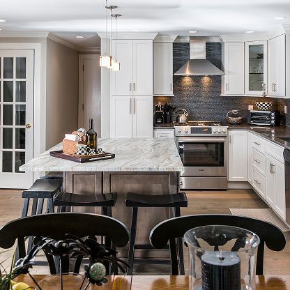 Modern white kitchen with marble island, dark stools, stainless appliances, and pendant lights