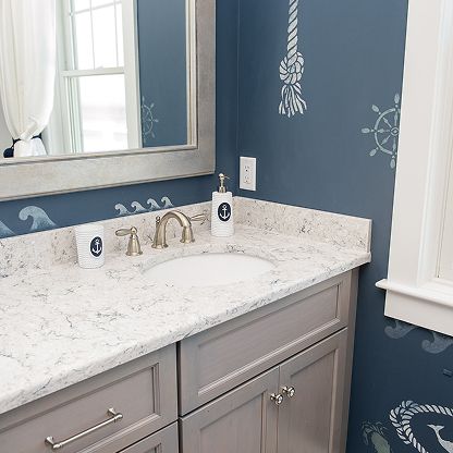 Blue bathroom vanity with white marble countertop, mirror, and sink under a window