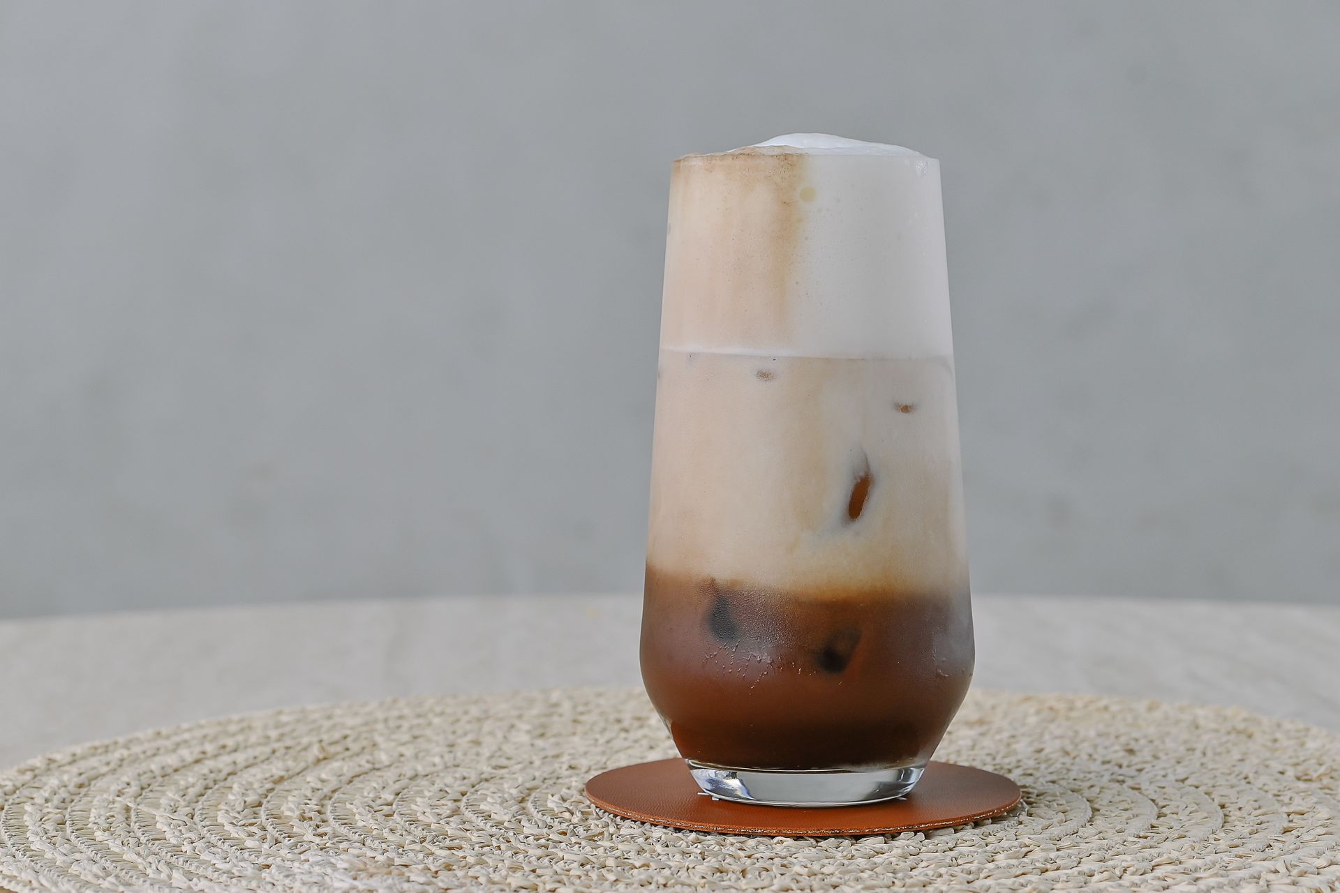 A glass of iced coffee is sitting on a coaster on a table.