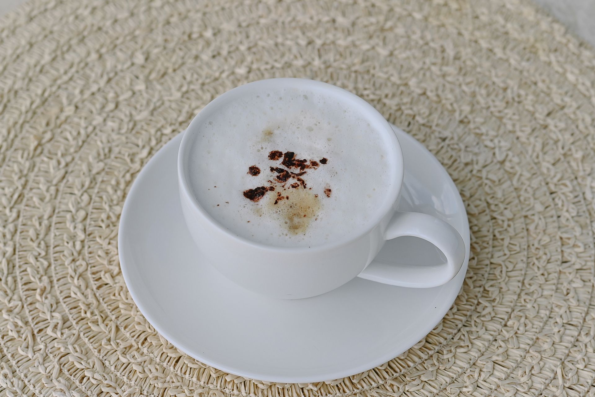 A cup of cappuccino on a saucer on a table.