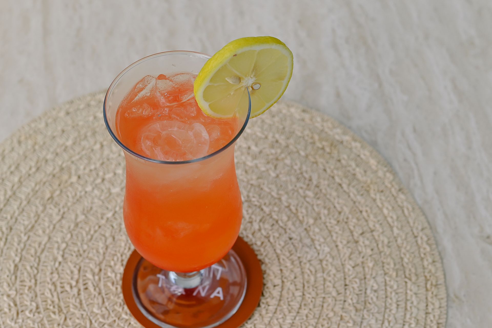 A glass of orange juice with ice and a slice of lemon on a table.