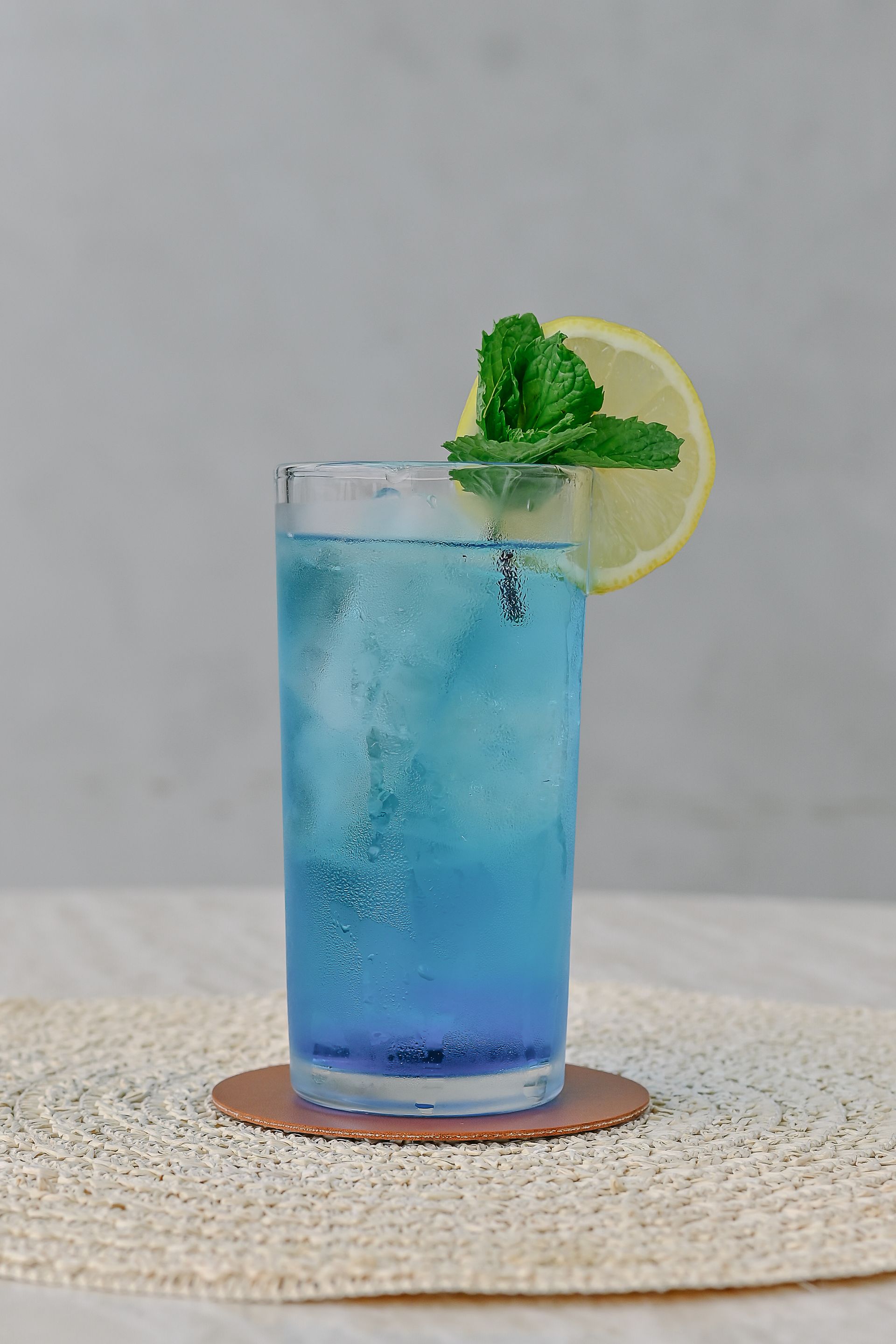 A blue drink with ice and a slice of lemon on a table.