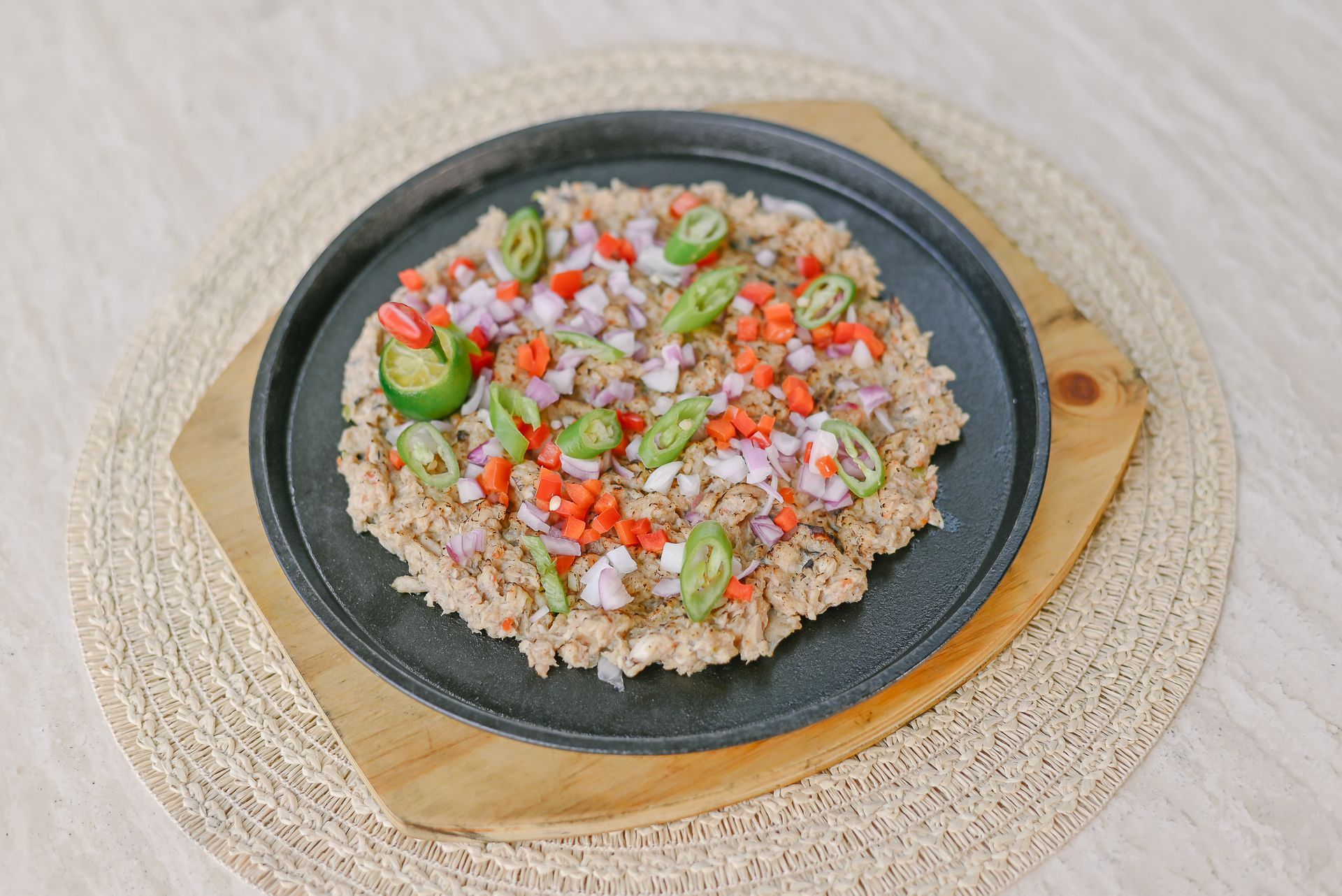 A black plate topped with rice and vegetables on a wooden cutting board.