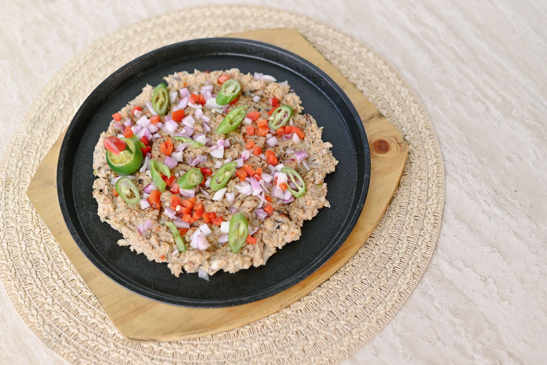 A pizza with onions , peppers , and tomatoes on a black plate on a wooden cutting board.