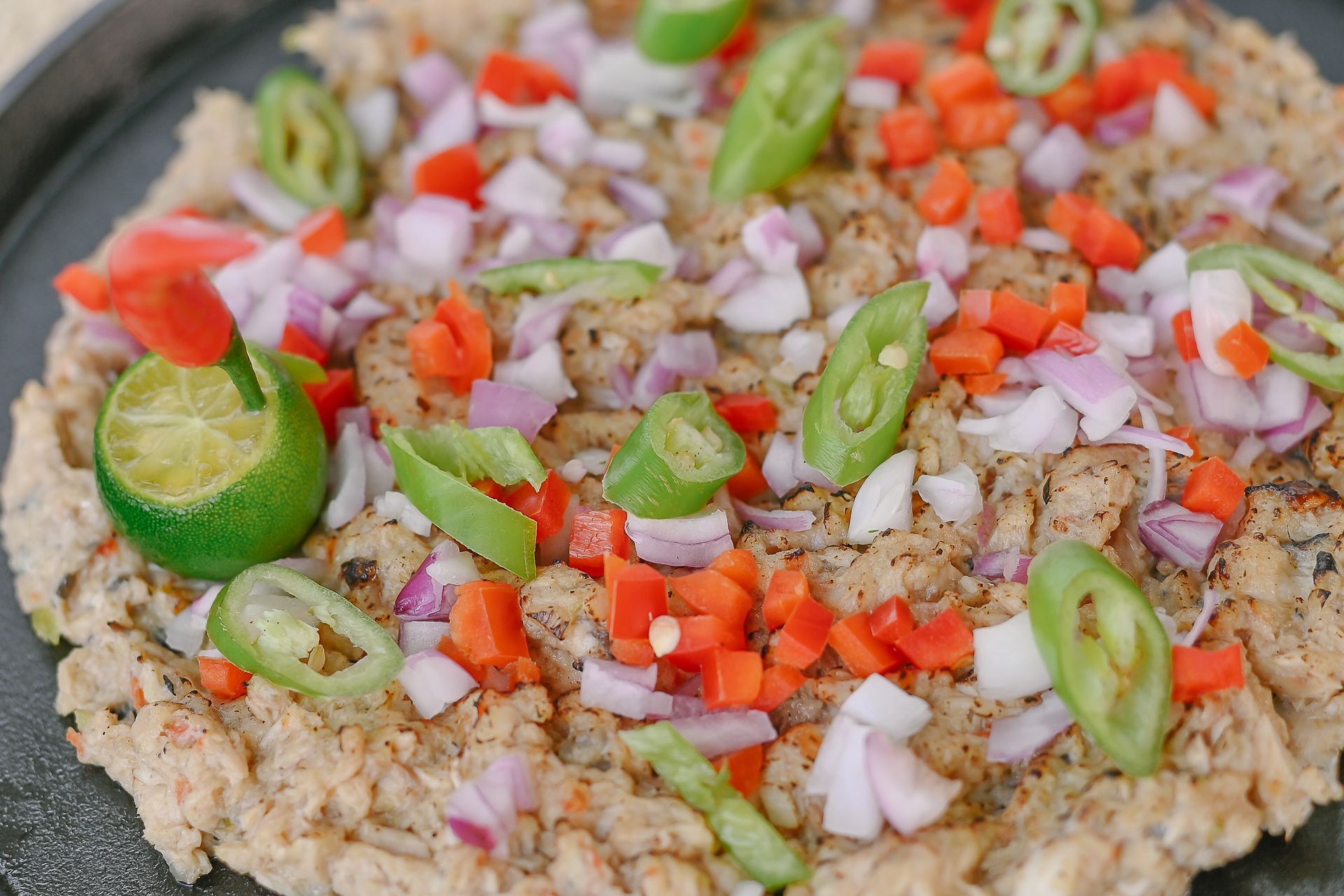 A pizza with onions , peppers , and limes on a black plate.