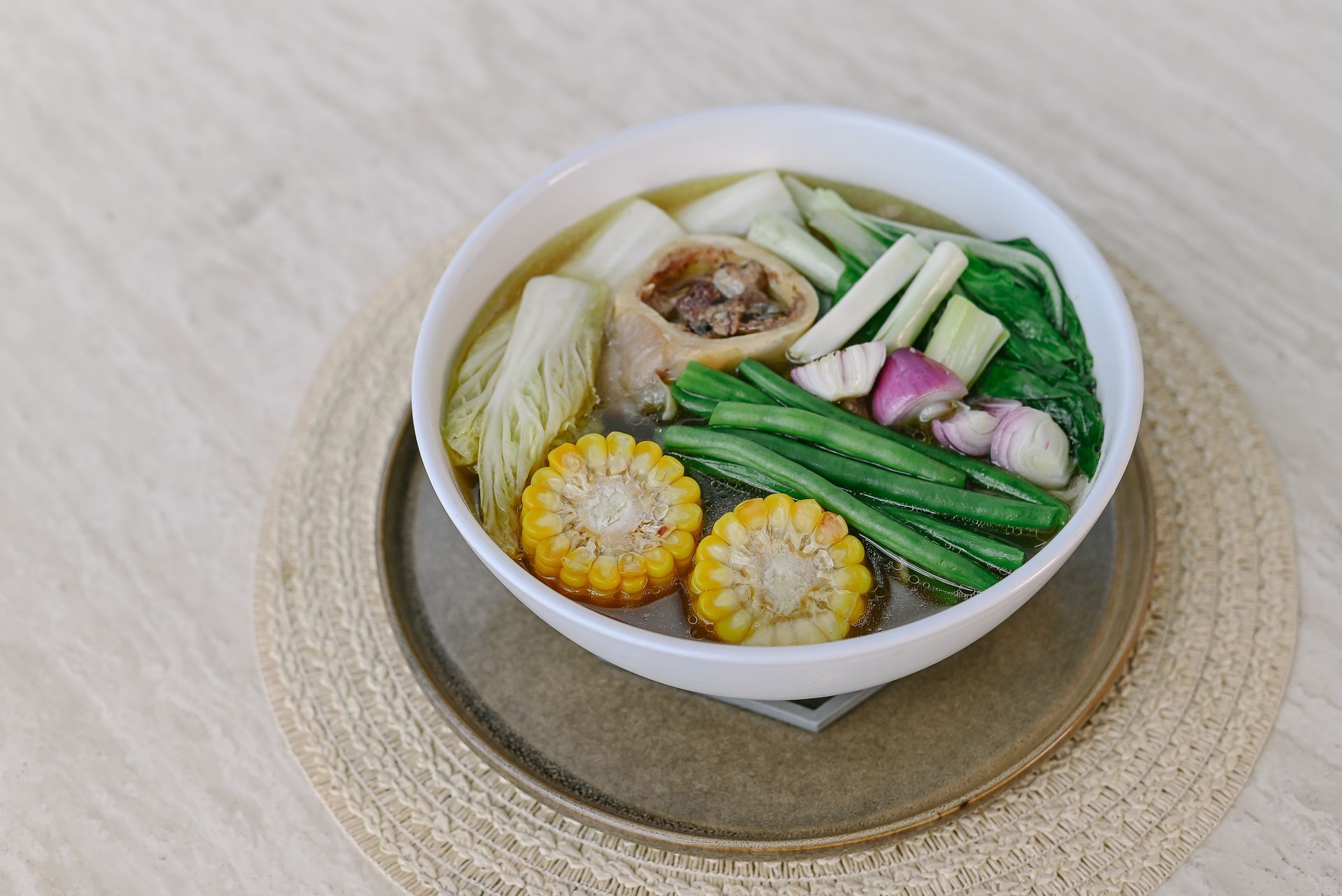 A bowl of soup with corn , green beans , cabbage and onions on a table.