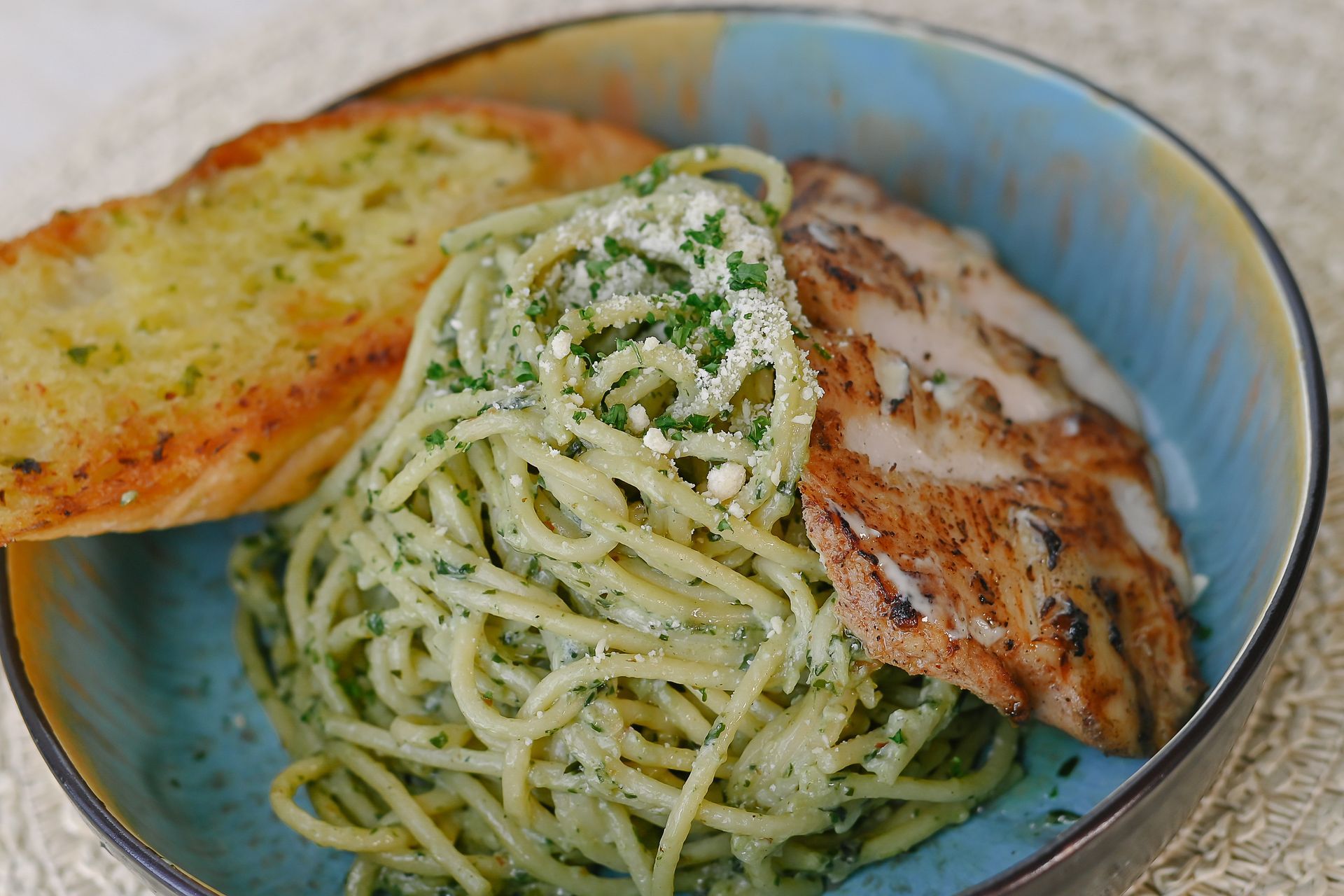 A bowl of spaghetti with chicken and garlic bread on a table.