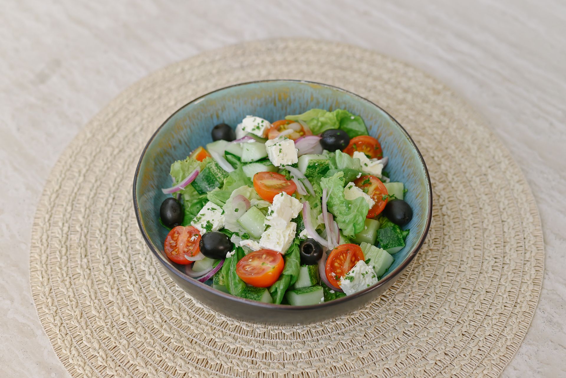 A bowl of salad with tomatoes , cucumbers , olives and feta cheese on a table.