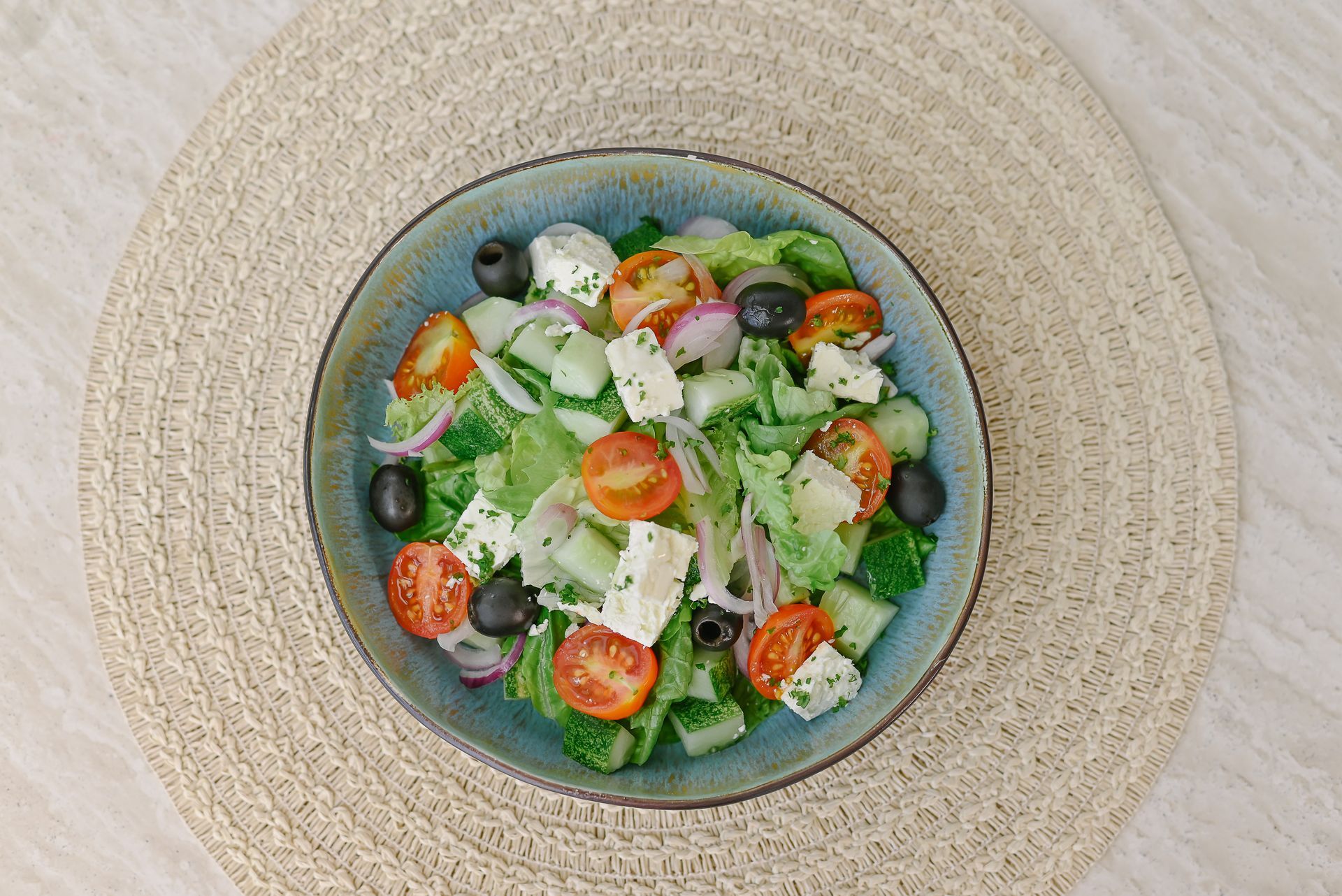 A bowl of salad with tomatoes , cucumbers , olives and feta cheese on a table.