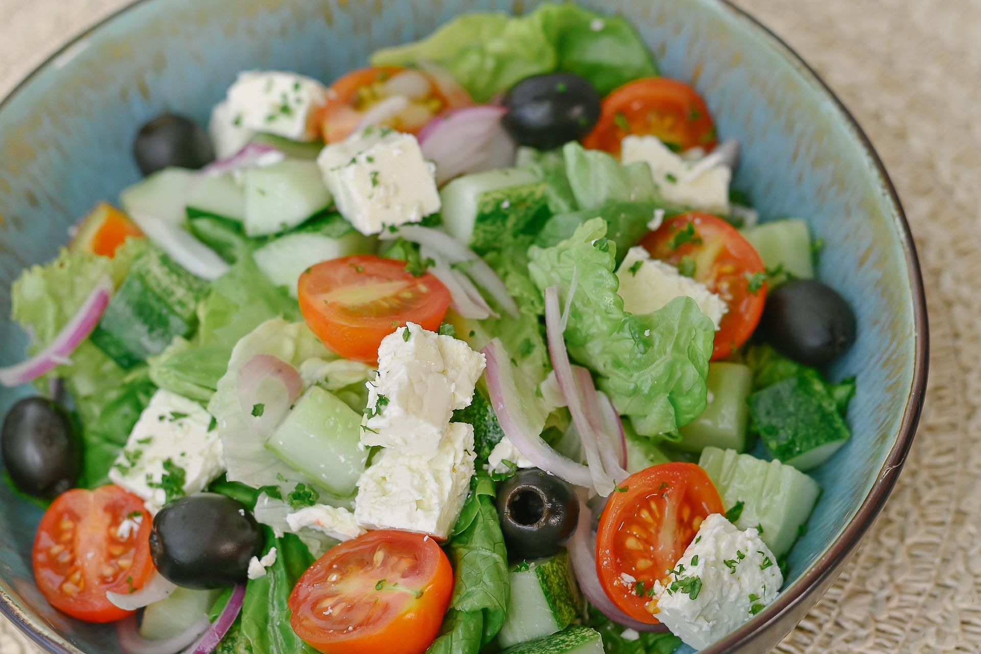 A salad with tomatoes , cucumbers , onions , olives and feta cheese in a bowl.