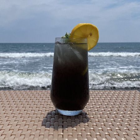 A tall glass of iced tea with a lemon slice on a table with the ocean in the background