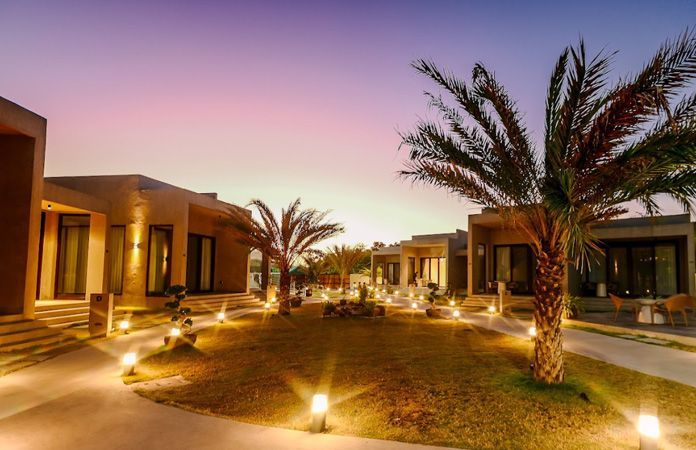 A row of houses with palm trees in front of them are lit up at night.