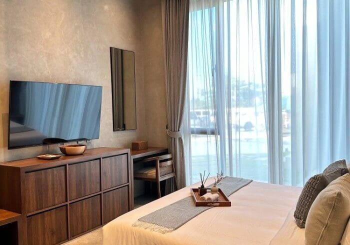 A bedroom with a bed , dresser , television and a large window.