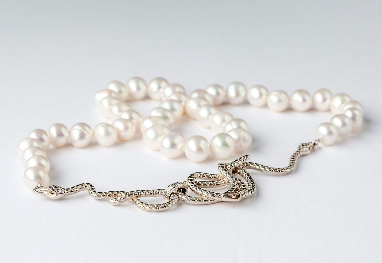 A pearl necklace with a silver chain on a white surface.