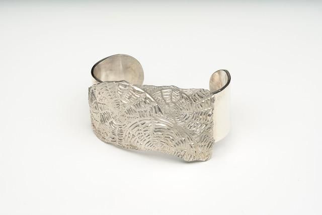A silver bracelet is sitting on a white surface.