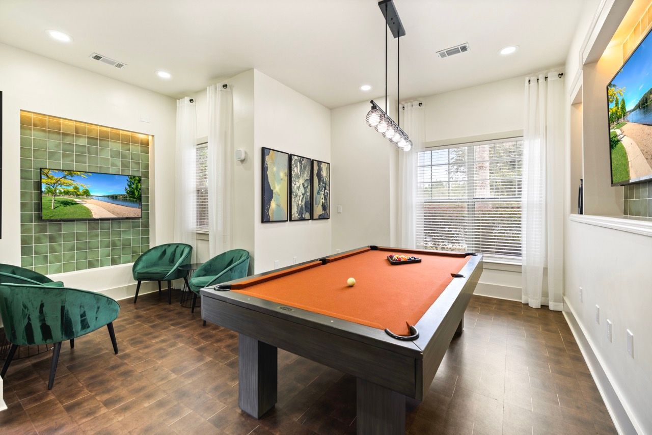 Indoor community game room with a pool table, green chairs, and wall-mounted TVs.