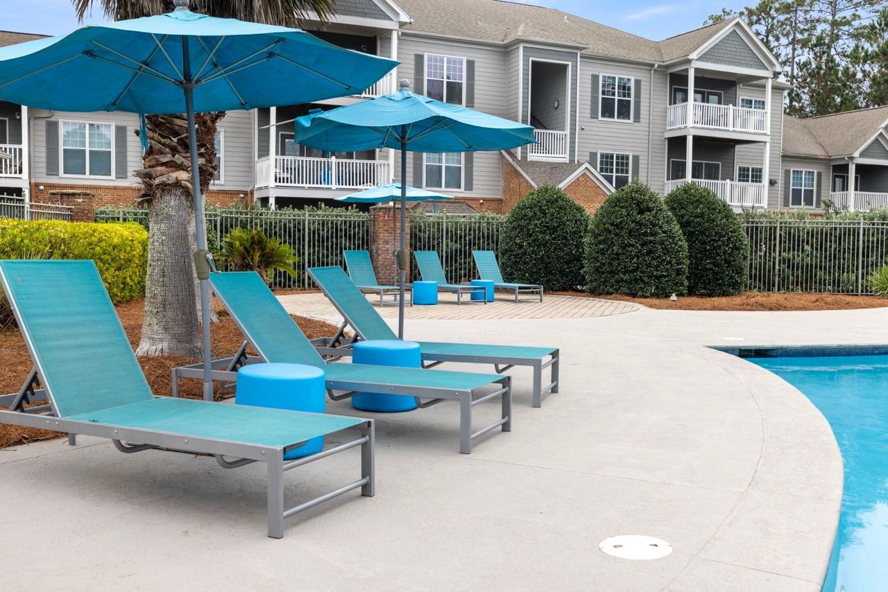 Outdoor pool area with turquoise lounge chairs and blue umbrellas.