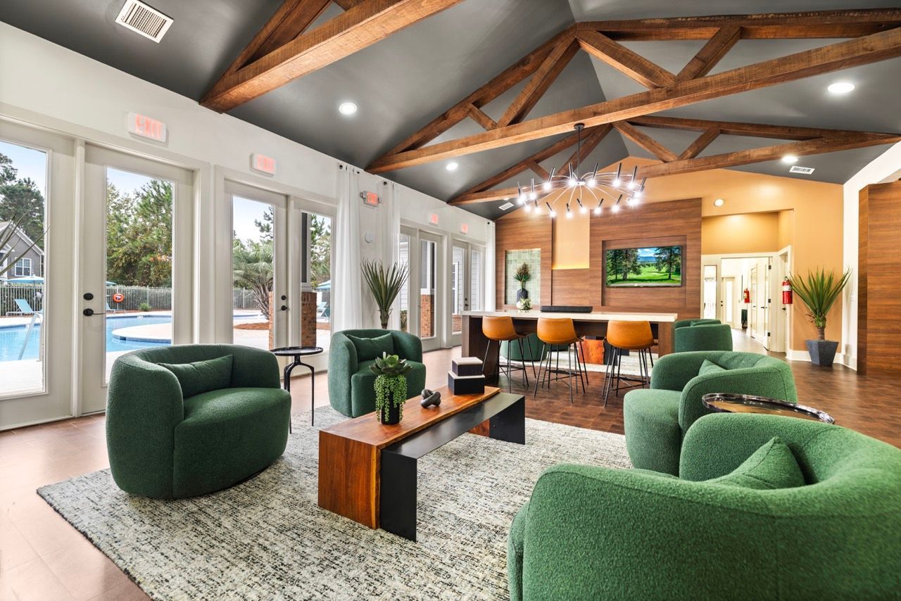 Spacious community lounge with green seating, a wood-beam ceiling, and a view of the pool.