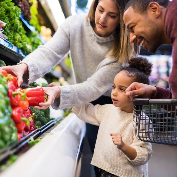 A family selects fresh red peppers from a grocery store display.