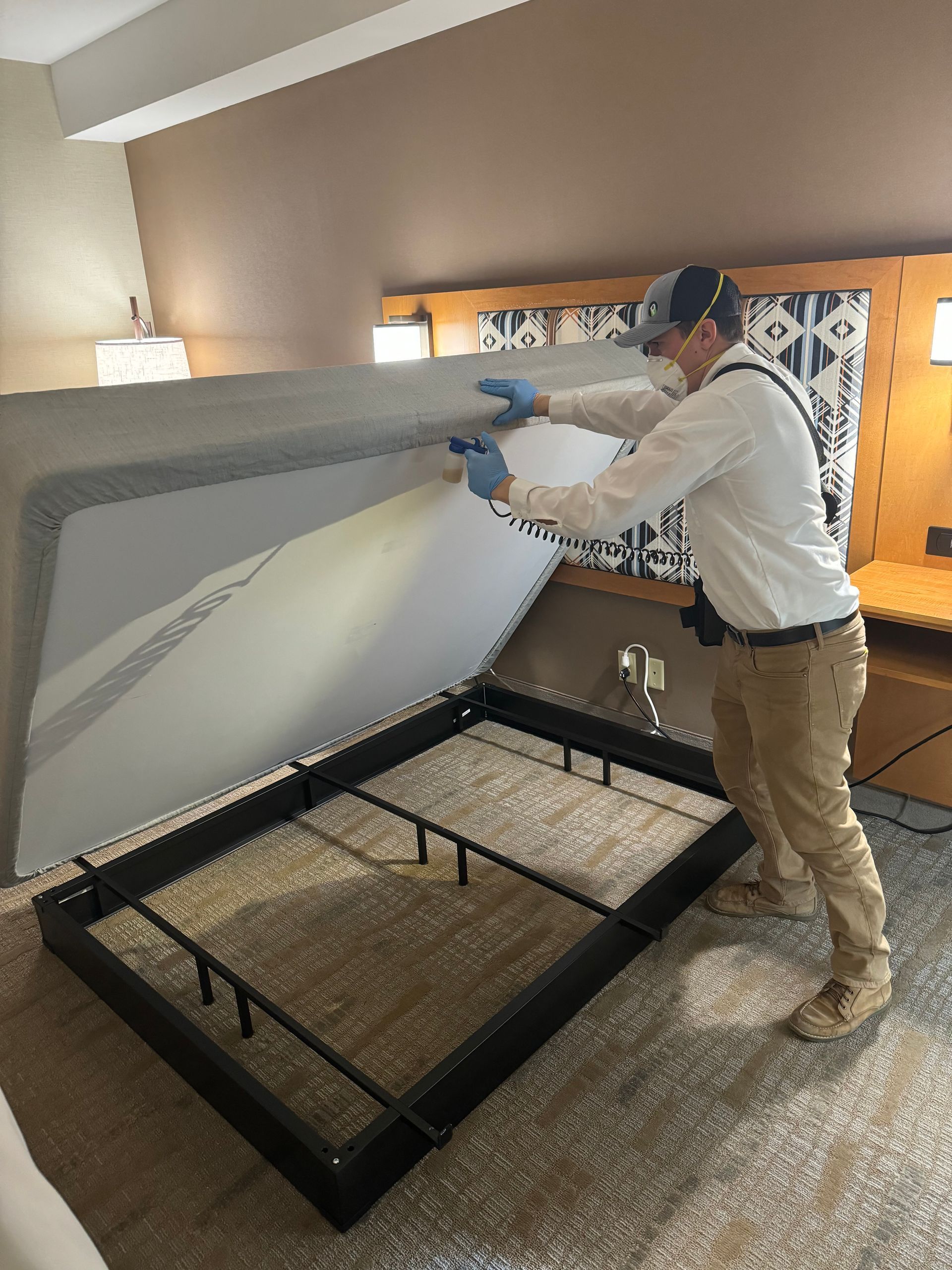 A man is cleaning a bed in a hotel room.