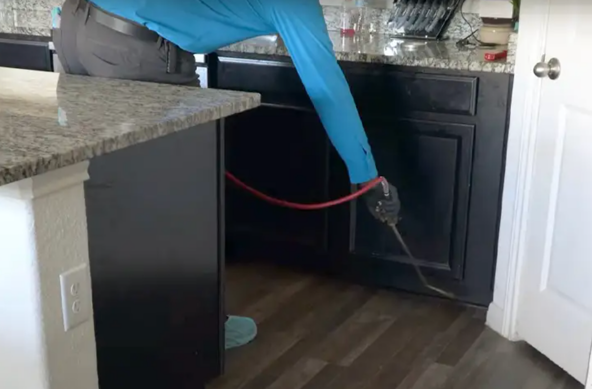 A pest control technician treating the baseboards of a kitchen