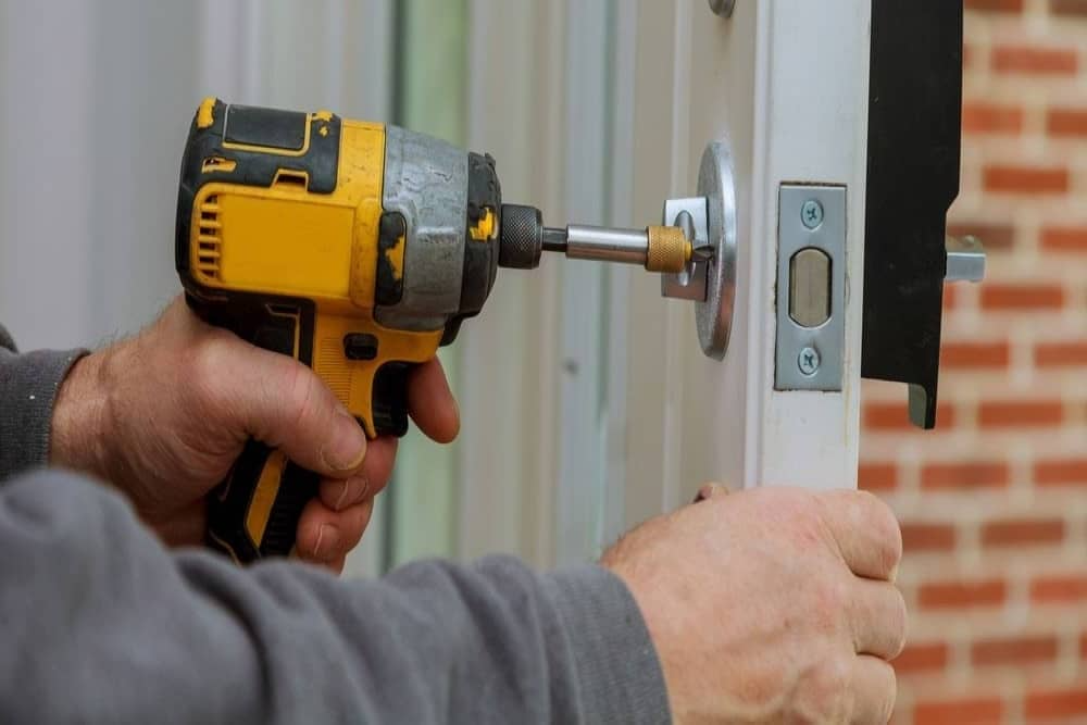 A man is using a drill to fix a door lock.
