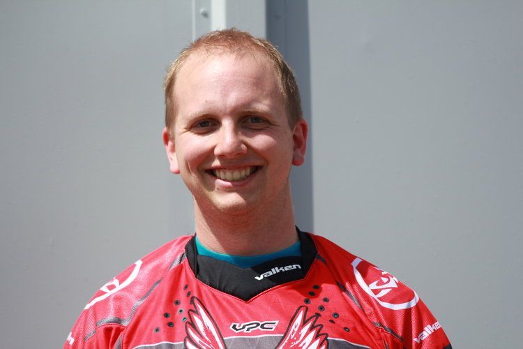 A man wearing a red shirt with wings on it is smiling