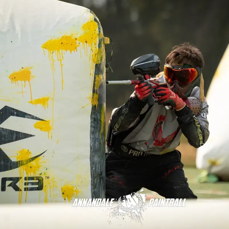 A man is playing paintball in front of a k3 paintball bag