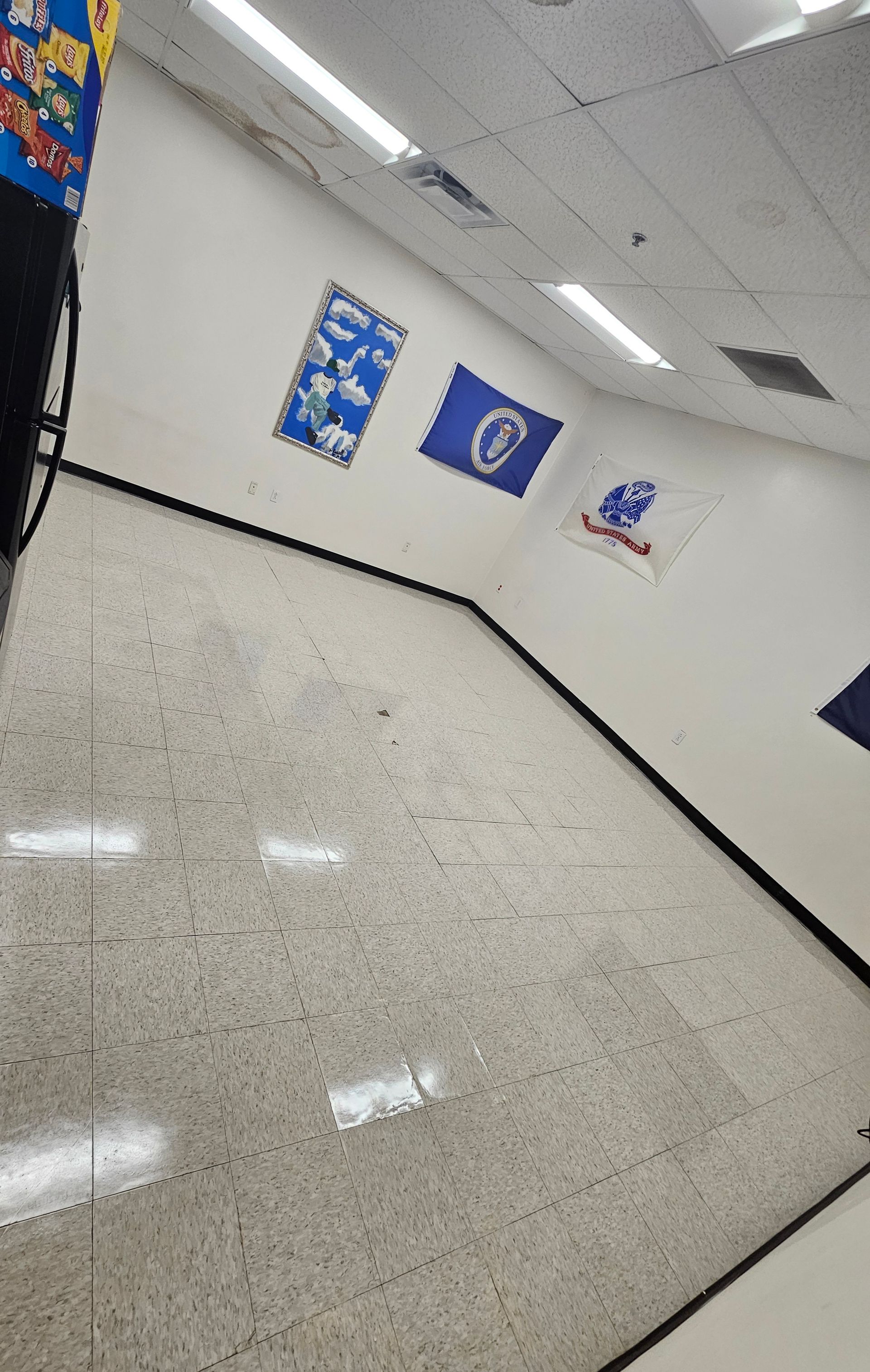 Tilted view of a bright hallway with white walls, terrazzo floor, and blue posters hanging near the ceiling