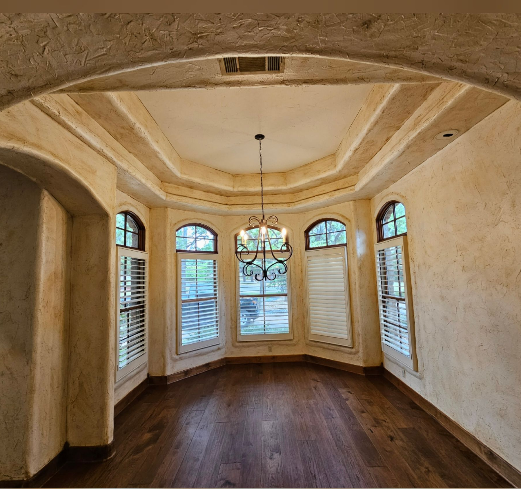 Empty elegant dining room with arched windows, chandelier, and dark wood floor
