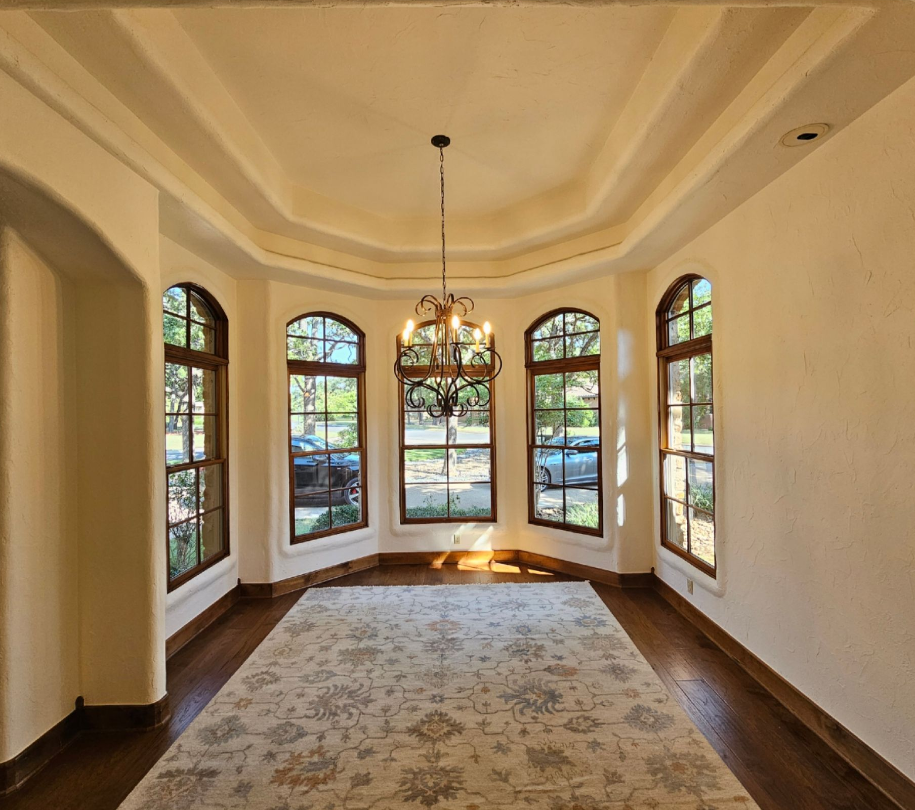 Empty sunlit room with bay windows, chandelier, and patterned rug