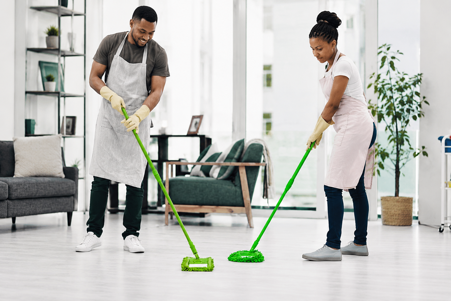 Two people mopping a bright living room floor with green cleaning tools