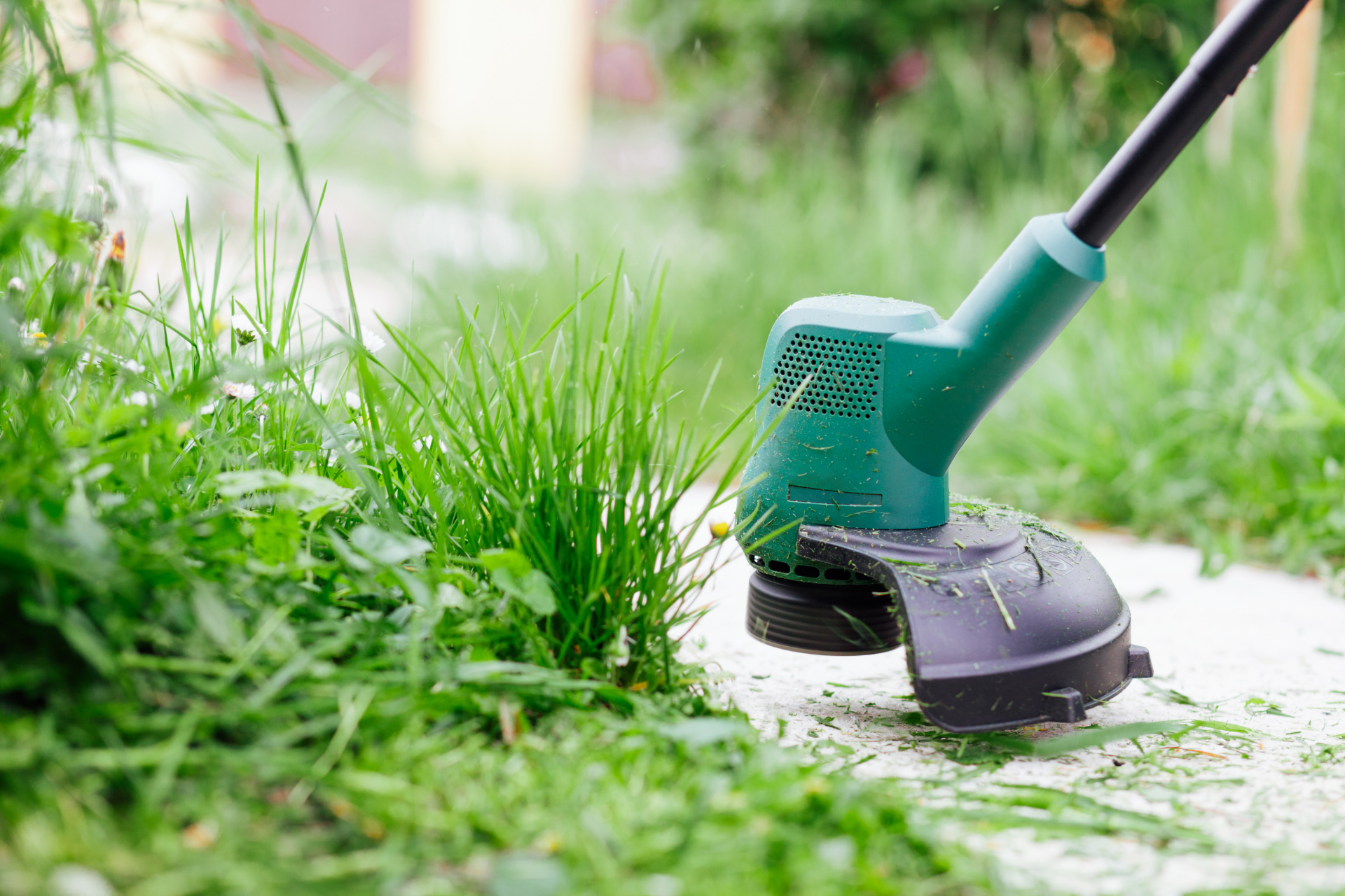 Green electric grass trimmer cutting weeds along a garden path