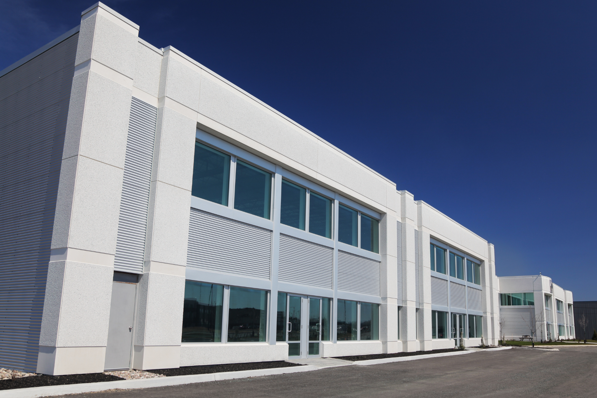White industrial building with large windows under a clear blue sky