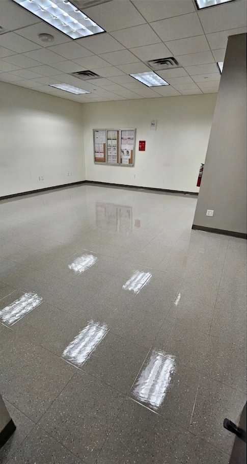 Empty office hallway with glossy tiled floor, beige walls, and bulletin boards under fluorescent lights