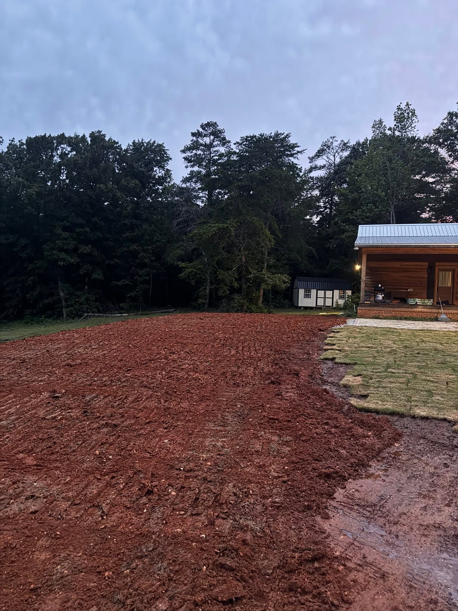 Freshly mulched yard beside a wooden cabin, with trees and an overcast sky in the background