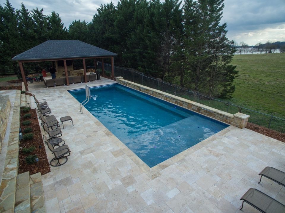 Inground swimming pool with raised wall and travertine decking