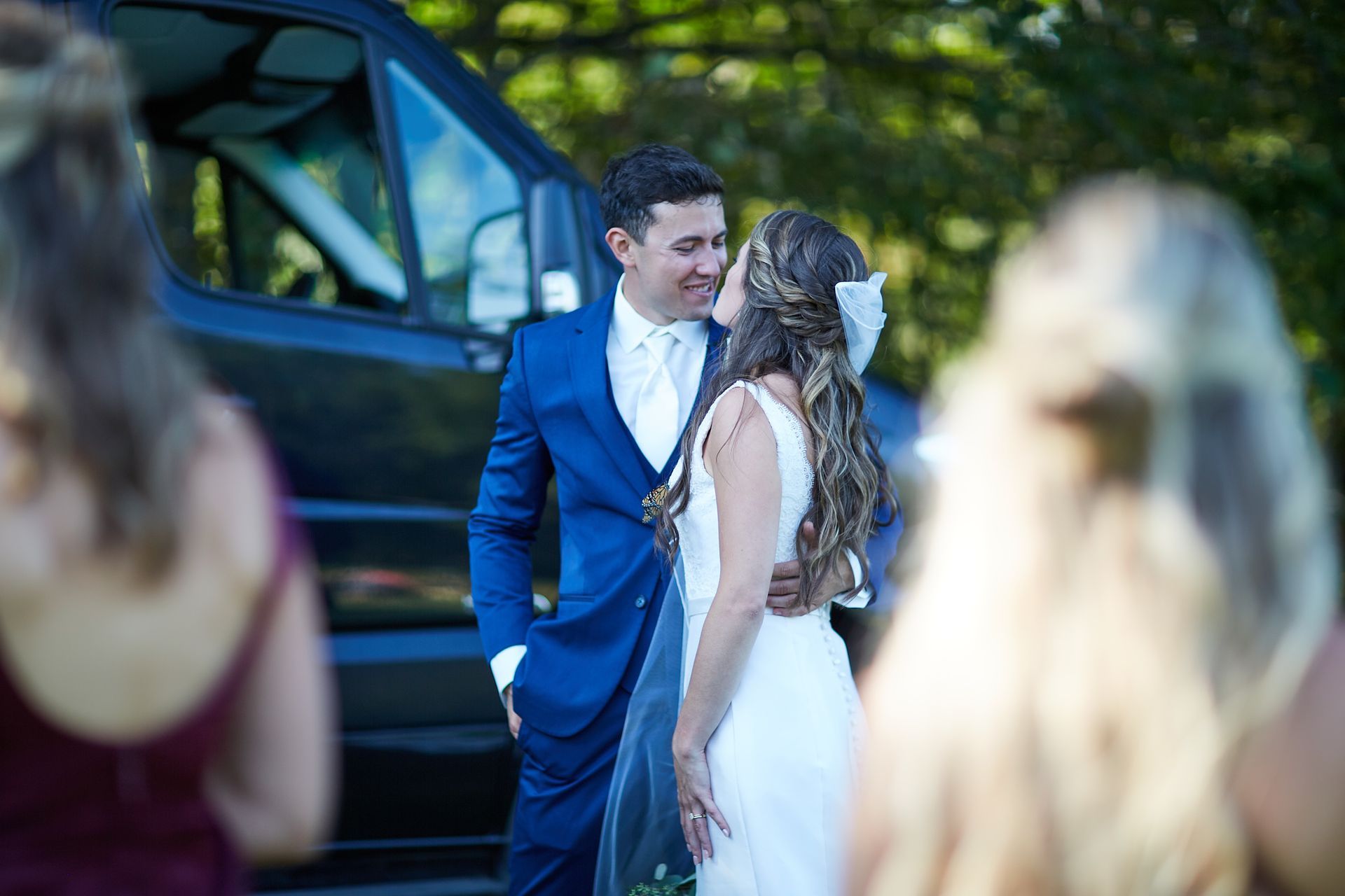 A bride and groom are kissing in front of a black van.
