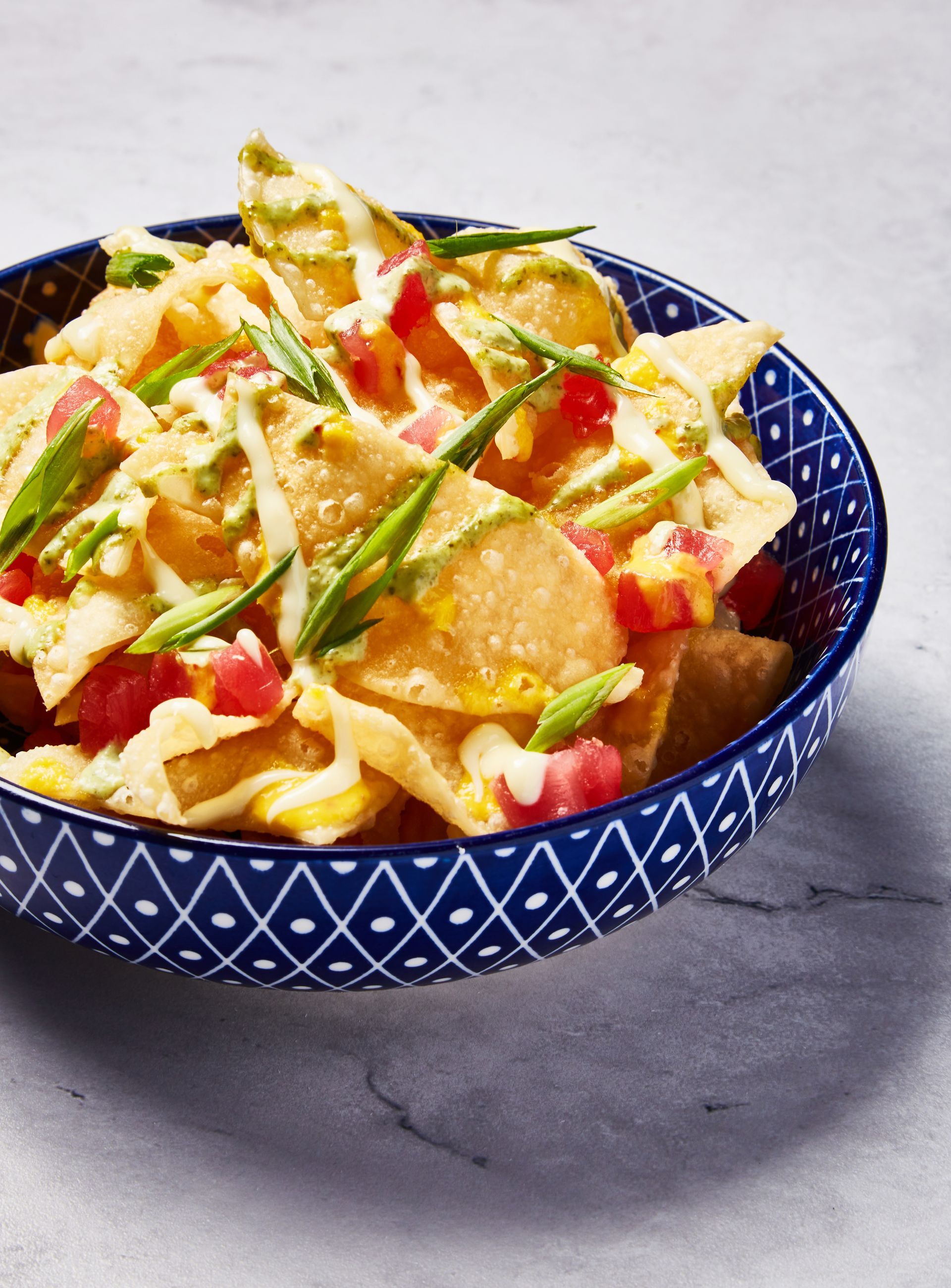A blue bowl filled with nachos and vegetables on a table.