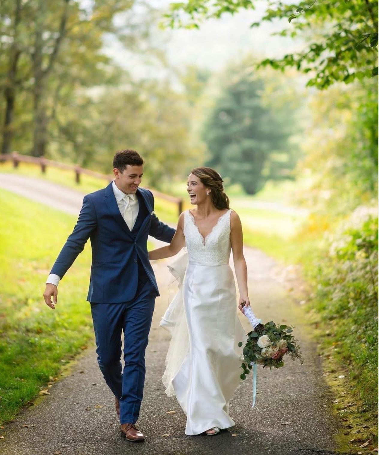 A bride and groom are walking down a path holding hands.