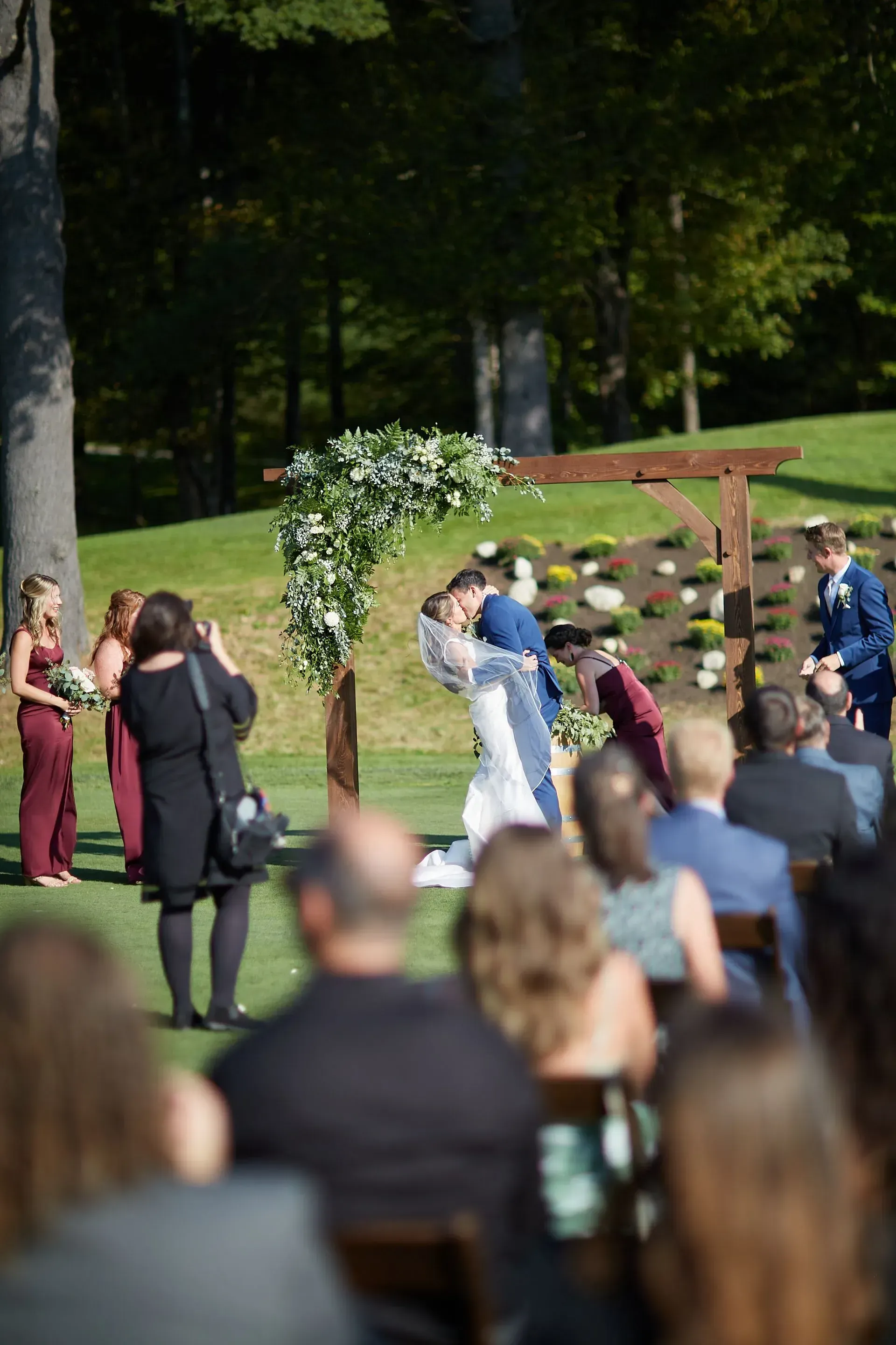 A bride and groom are kissing during their wedding ceremony while their guests watch.