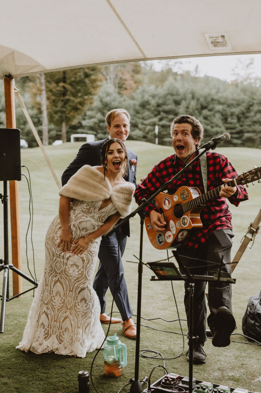 A bride and groom are standing next to a man playing a guitar and singing into a microphone.