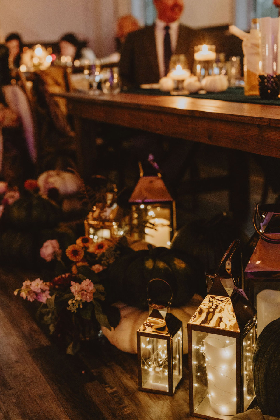 A group of people are sitting at a table with lanterns and flowers.