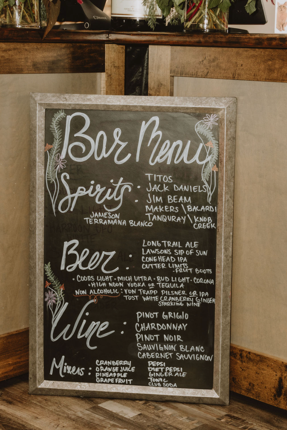 A bar menu is written on a blackboard in front of a wooden bar.