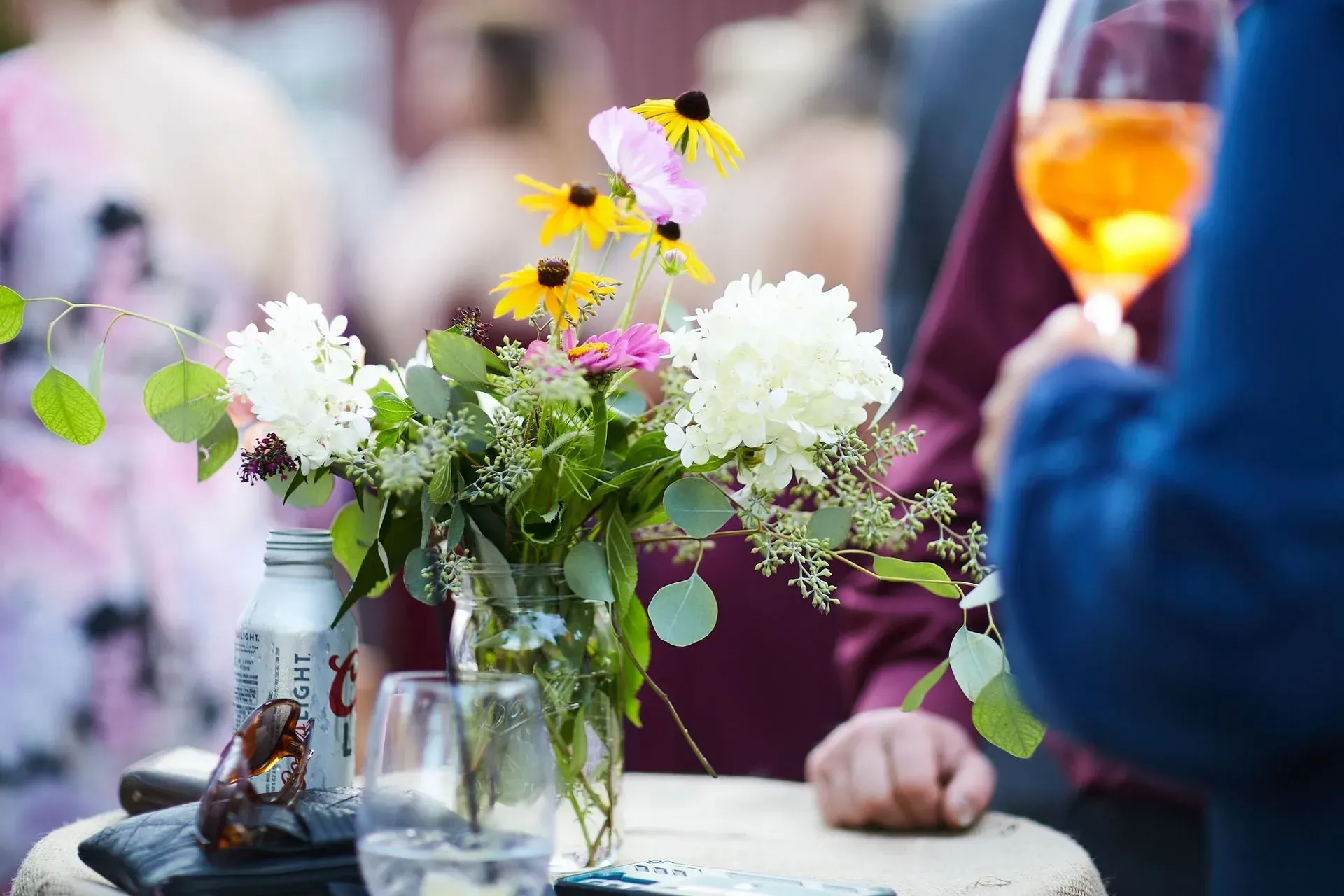 A vase of flowers is sitting on a table next to a glass of wine.