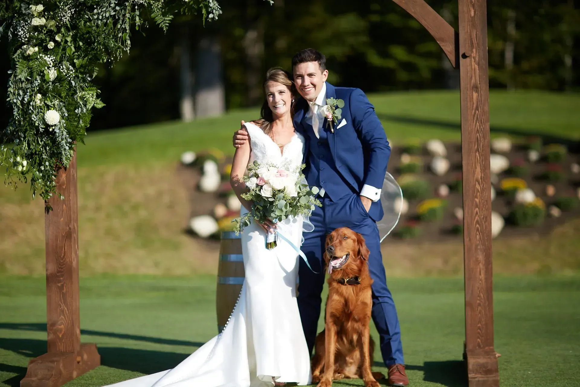 A bride and groom are posing for a picture with their dog at their wedding.