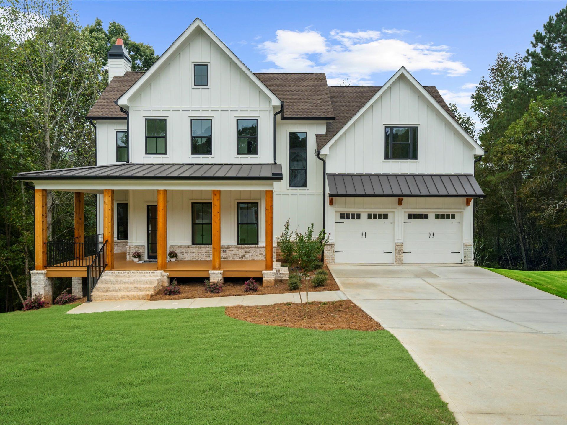White two-story house with a front porch, detached garage, and green lawn under a clear sky