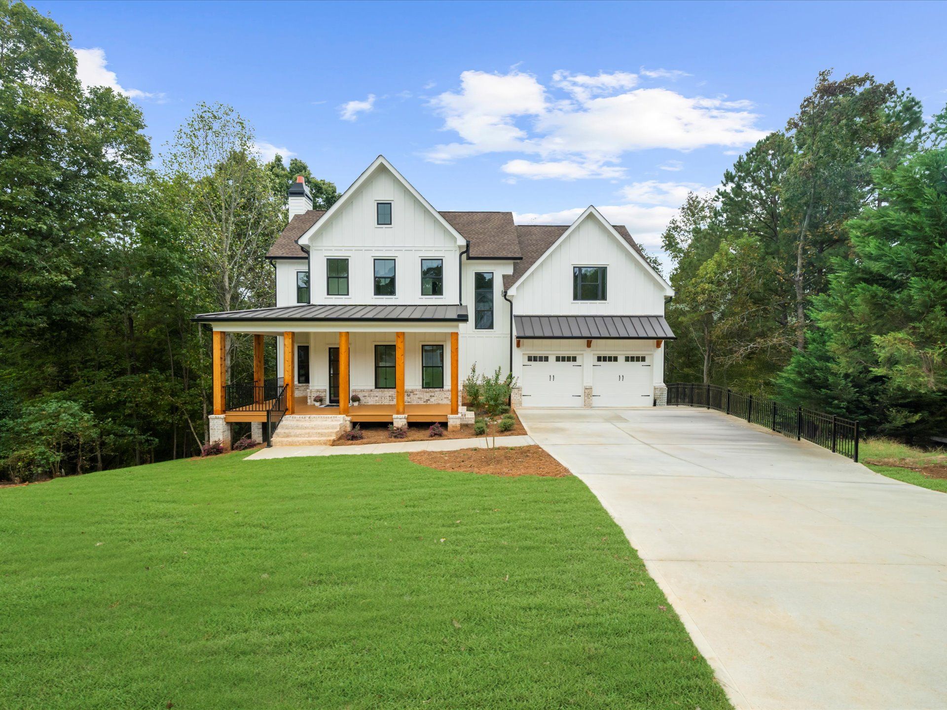 White two-story house with porch, garage, and large driveway surrounded by green trees and lawn