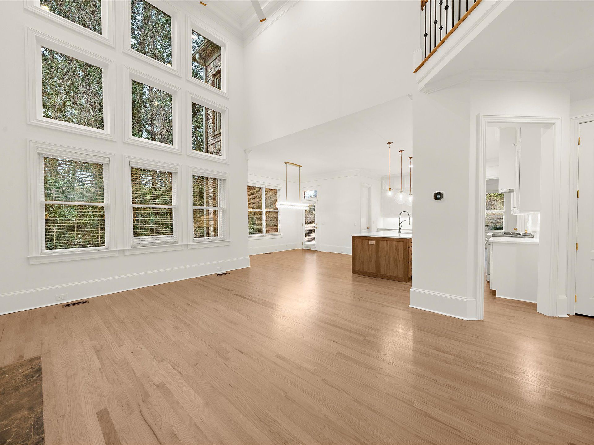 Bright empty living room with large windows, light wood floors, and white walls